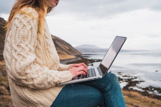 Iceland, woman using laptop at the coast